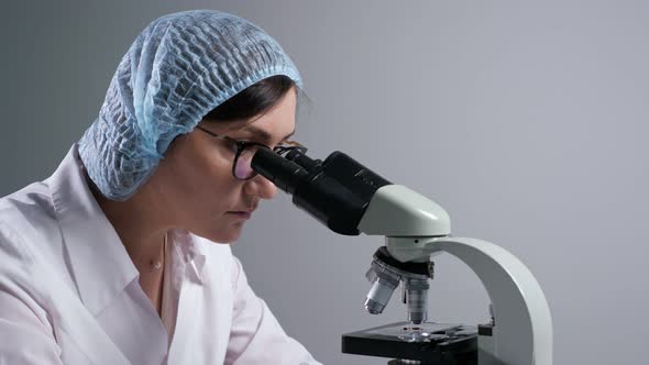 Scientist with Glasses Looks at Sample Through Microscope