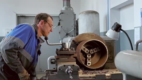 Metal Turner with Glasses Works at Lathe in Production Hall