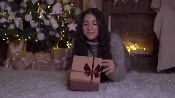 The Girl Opens the Box with a Gift and Rejoices Lying on the Floor Near the Christmas Tree