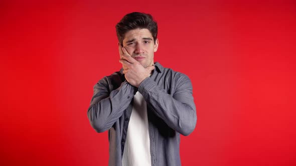 Young Man in Denim Shirt with Tooth Pain on Red Studio Background. Toothache