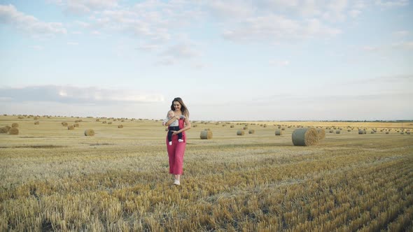 Happy Mother Walks and Whirls with Her Lovely Little Baby Boy on Hands in Field