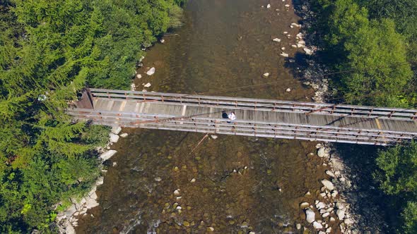 Aerial View From Old Wooden Suspension Bridge Over a Mountain River. Girl Standing on a Wooden