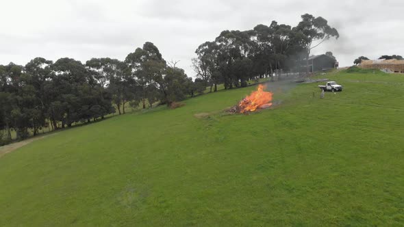 Aerial shot moving forward and flying over a big bonfire on a rural property with a white truck and