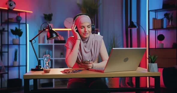 Muslim Woman in Headscarf Enjoying Favourite Music in Headphones from Phone Playlist at home