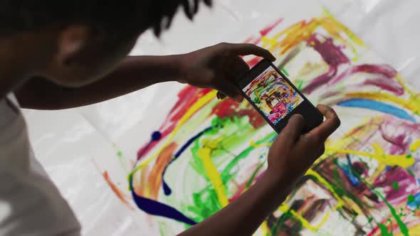 African american male artist taking a picture of his painting with a smartphone at art studio
