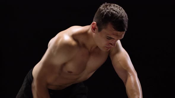 Man Flexes His Hands with Dumbbells Training His Back on a Black Background in the Studio