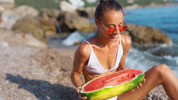 Joyful Girl in Bikini Holding Huge Slice of Watermelon Sitting on Sea Beach at Seaside