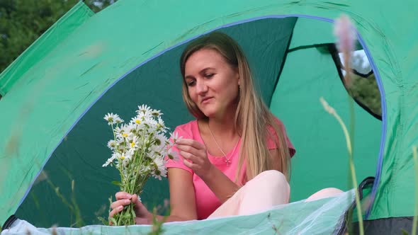 Beautiful girl holding a bouquet of daisies sitting in a tent.