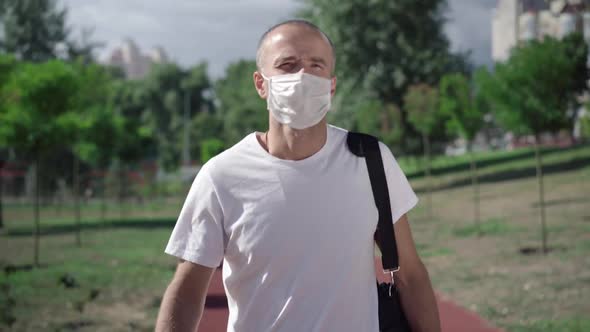 Adult Caucasian Sportsman Walking with Sport Bag, Taking Off Covid Face Mask, and Looking at Camera