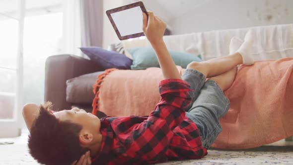 Happy asian boy at home, lying on floor in living room using tablet