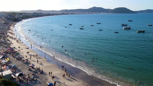 Aerial drone view of tropical beach with many people enjoying the sand and sea in late afternoon