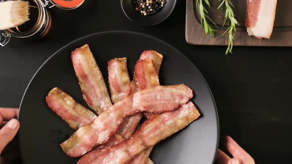 Cooked bacon strips on a black plate.