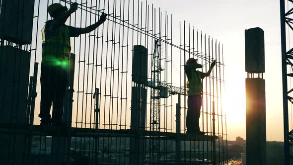 People Work with Metal Poles at a Construction Site. alt