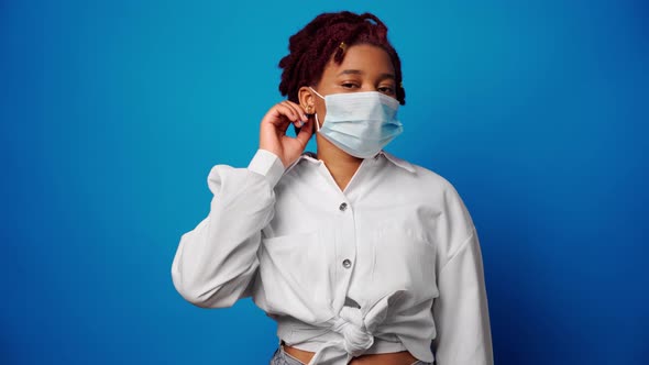 Young Afro Woman Takes Off Medical Mask and Smiles Against Blue Background