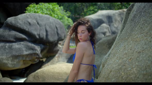 Brunette Woman in Blue Swimwear Posing on the Beach Against the Rocks