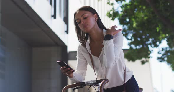 African american woman using smartphone leaning on bike in street