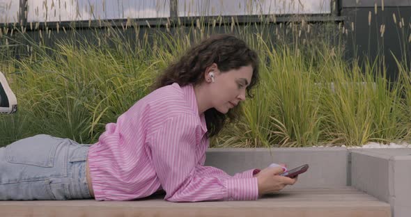 Happy European teen having fun and lying on the bus stop with a smartphone.