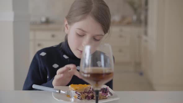 Pretty Blond Girl Sitting at the Table in the Kitchen Eating Cake with Her Fingers