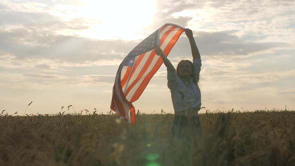 Happy Patriotic Young Woman Waves the US Flag Into the Field