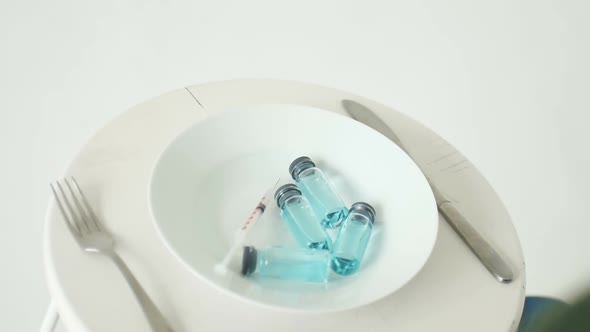 Woman is Going to Eat From White Plate with Glass Ampoules with Blue Liquid Inside Vaccination