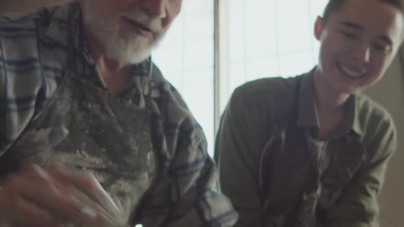 Senior Potter Teaching Young Woman How to Make Ceramic Pot