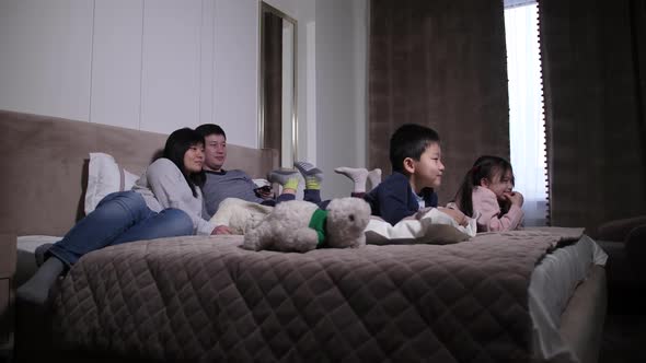 Happy Asian Family with Kids Watching TV on Bed