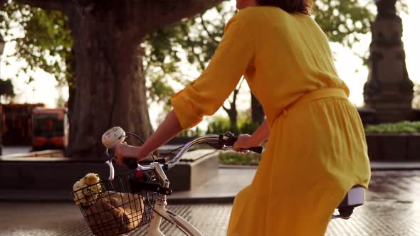 Back View of an Unrecognizable Woman Riding a Citybike with a Basket and Flowers in the City Park