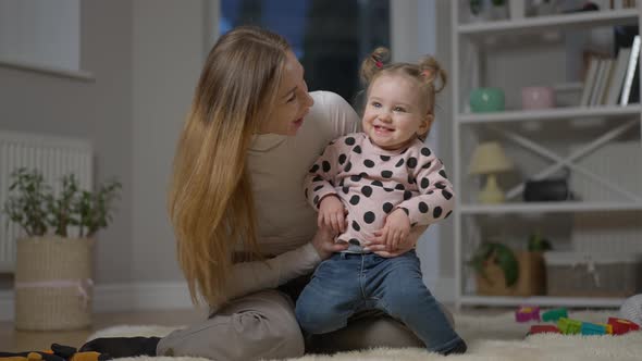 Wide Shot of Cheerful Funny Young Mother Playing with Baby Daughter Having Fun at Home