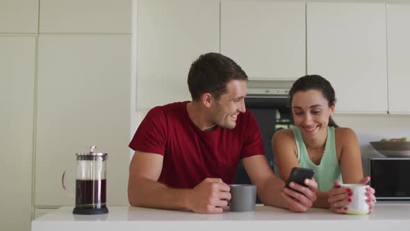 Happy caucasian couple drinking coffee and using smartphone