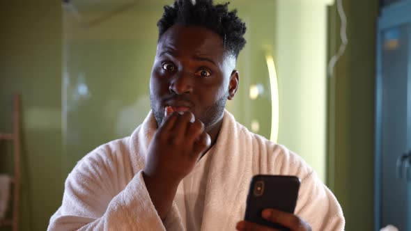 Young Handsome African American Man Brushing Teeth Watching Videos in Social Media on Smartphone