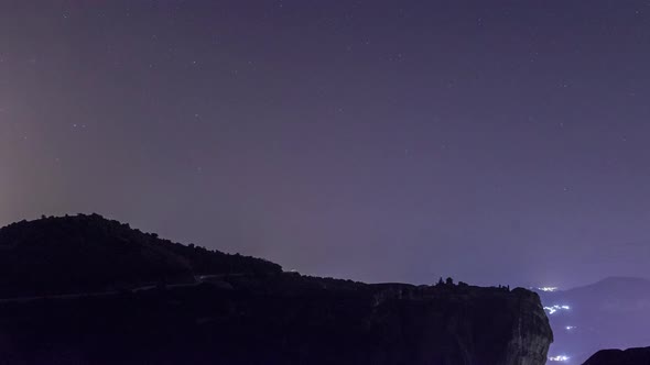 Time lapse of stars moving on the nightsky over silhouette of rock and Monastery, Greece