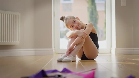 Charming Caucasian Teenage Gymnast Dreaming Smiling Hugging Knees Sitting on Floor Indoors