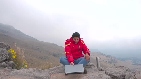 Young man sitting on a rock ad using a laptop and to drink coffe