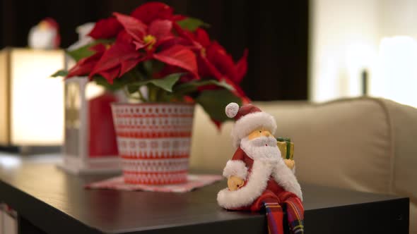 A Santa Claus Figure Sits on the Edge of a Table in a Christmas-decorated Apartment