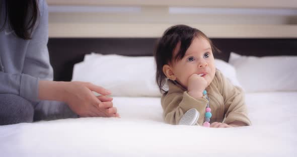 Baby Lies on Her Stomach on the Bed in the Nursery and Licks the Nipple Holder