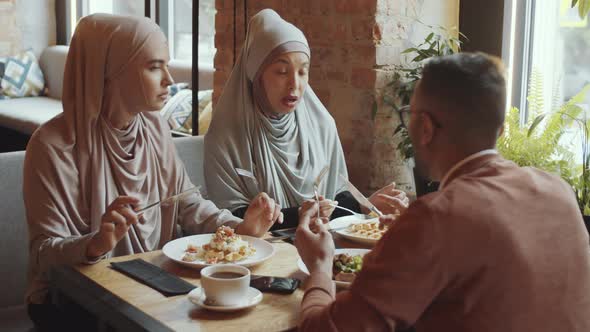 Muslim Women Having Lunch and Talking with Male Friend in Cafe