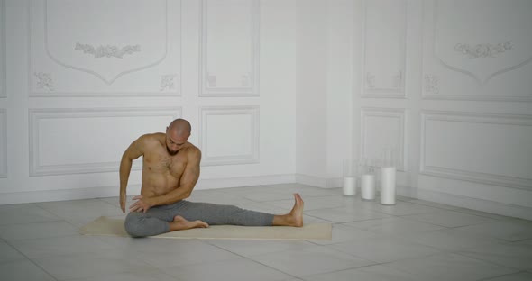 Man Is Performing Exercises for Stretching His Body and Muscles, Sitting on Floor Mat