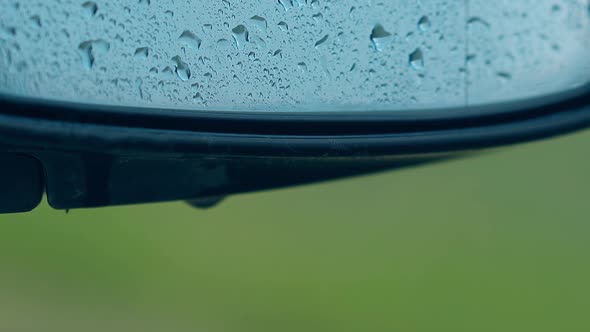 Close Side Mirror with Water Drops Against Blurred Grass