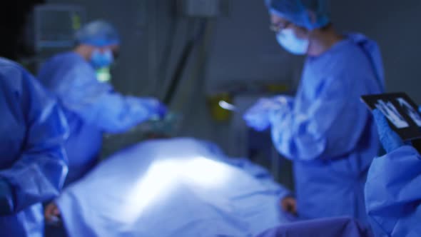 Diverse group of surgeons wearing face masks and protective clothing using tablet during operation