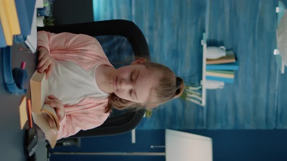 Vertical Video Caucasian Girl Reading Book at Desk for Primary School Work