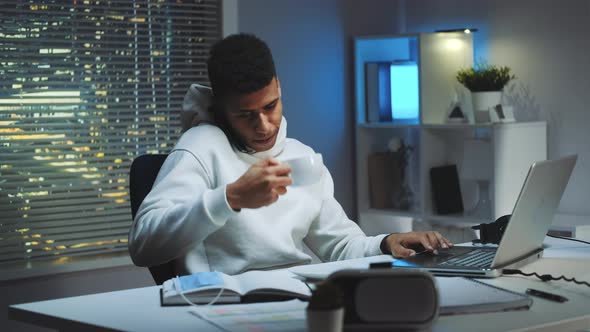 Mixed-race Man Working on Computer, Speaking By Smartphone and Drinking a Cup of Tea