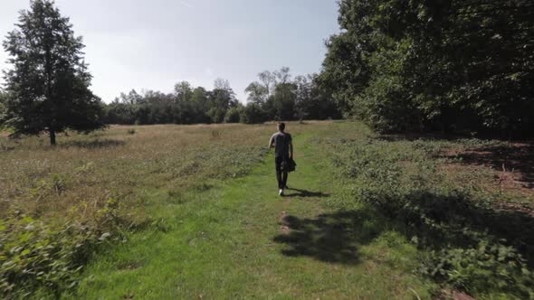 Caucasian man with bag slung over one shoulder walking through field in Trent Park North London UK l