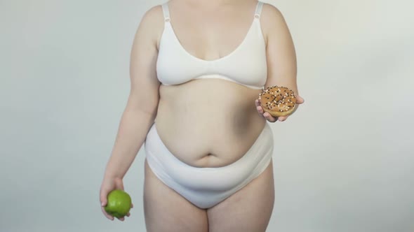 Corpulent Woman in White Lingerie Showing Apple and Donut Before Camera, Choice