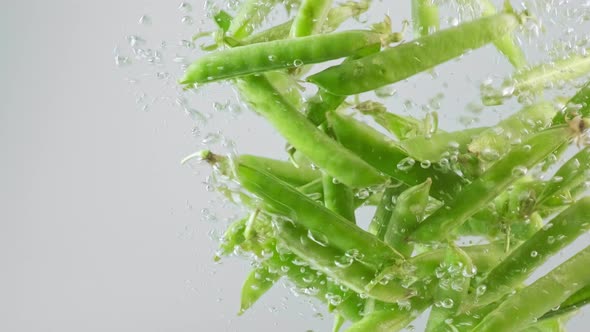 Green pods peas falling in clear water. Healthy food concept