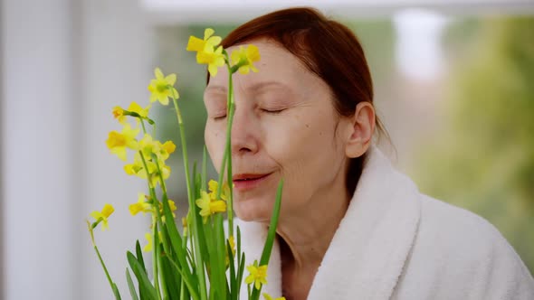 Closeup Happy Mature Woman Smelling Yellow Flowers Smiling Standing at Home in Living Room