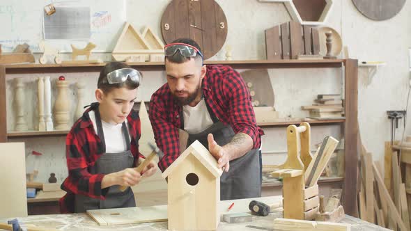 Father and His Son Working Together in a Wooden Workshop, Building a Birdhouse