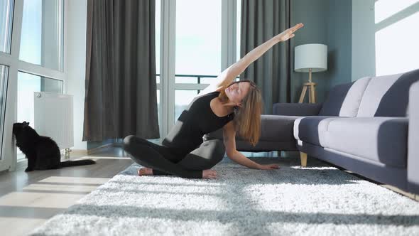 Young Caucasian Woman in Black Jumpsuit Doing Yoga at Home to Develop Flexibility and Balance