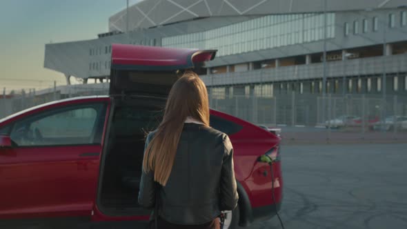 Close Up of a Girl Approaches an Electric Car Which is Charging at the Station