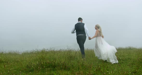 Luxury Couple Running on the Mountain Meadow on the Background of the Fog and Falling Rain. Slow