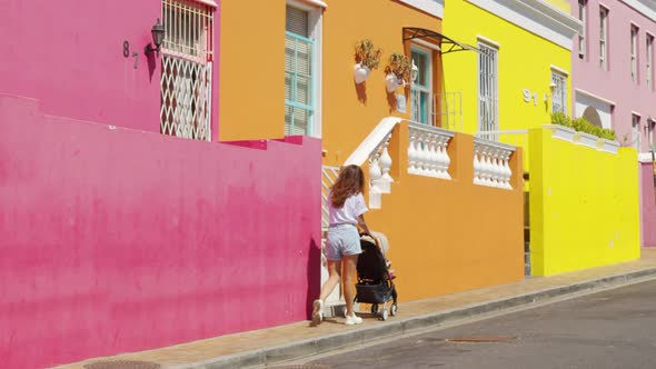 Woman Walking with Baby Stroller in the Streets of Colorful Buildings Neighbourhood BoKaap Cape Town